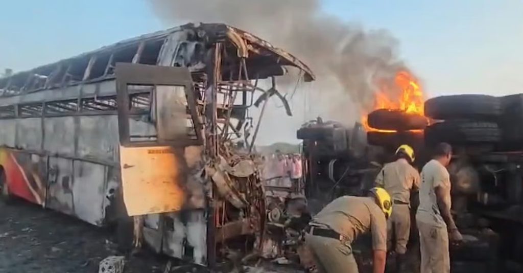 Charred remains of a private sleeper bus and a tipper truck at the accident site in Rayavaram, Markapuram, surrounded by emergency responders.