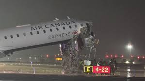A Bombardier CRJ-900 regional jet on a runway at night with severe damage to its nose and cockpit after colliding with an airport fire truck.