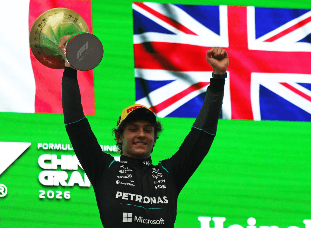 A jubilant 19-year-old Kimi Antonelli in a Mercedes race suit holding the first-place trophy on the podium at the Shanghai International Circuit.