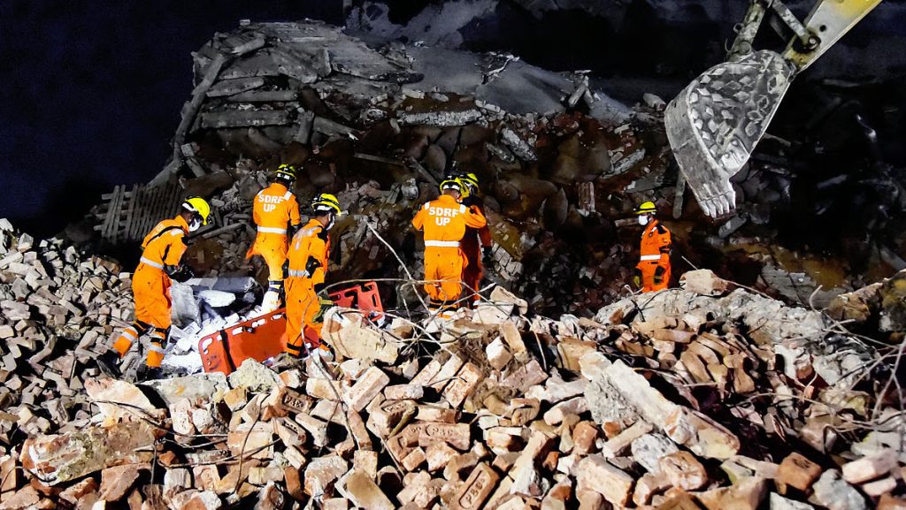 Rescue workers from NDRF and SDRF navigating the debris of a collapsed cold storage building in Phaphamau, Prayagraj, amidst white ammonia gas fumes.